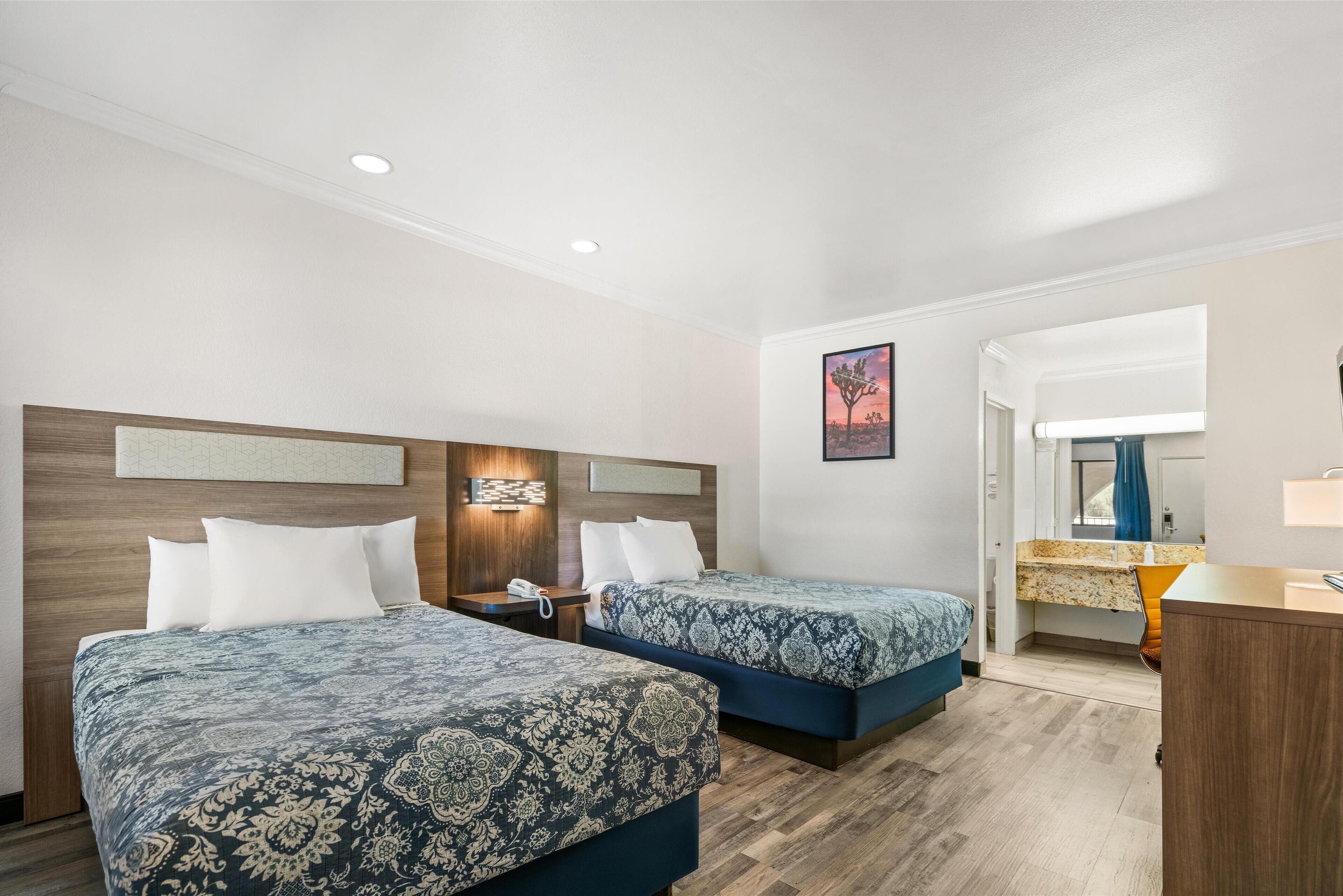 A hotel room with two beds, a wooden headboard, a small desk, and a bathroom visible through an open door.
