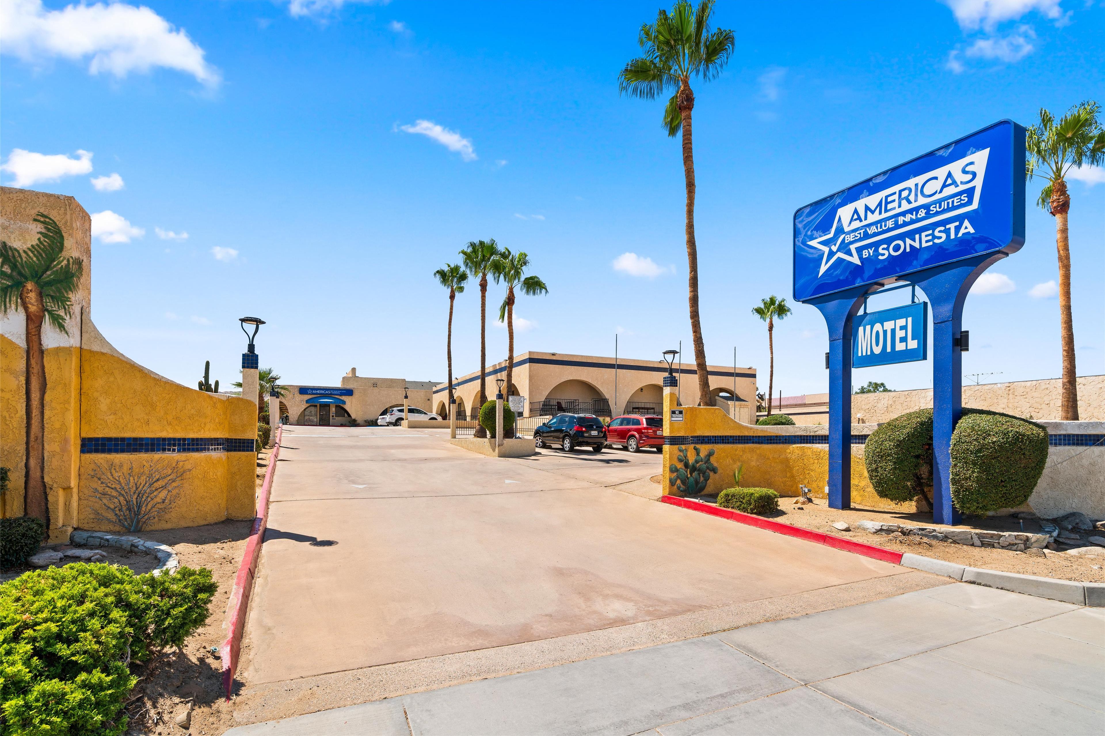 A motel sign with a palm tree and a building in the background.