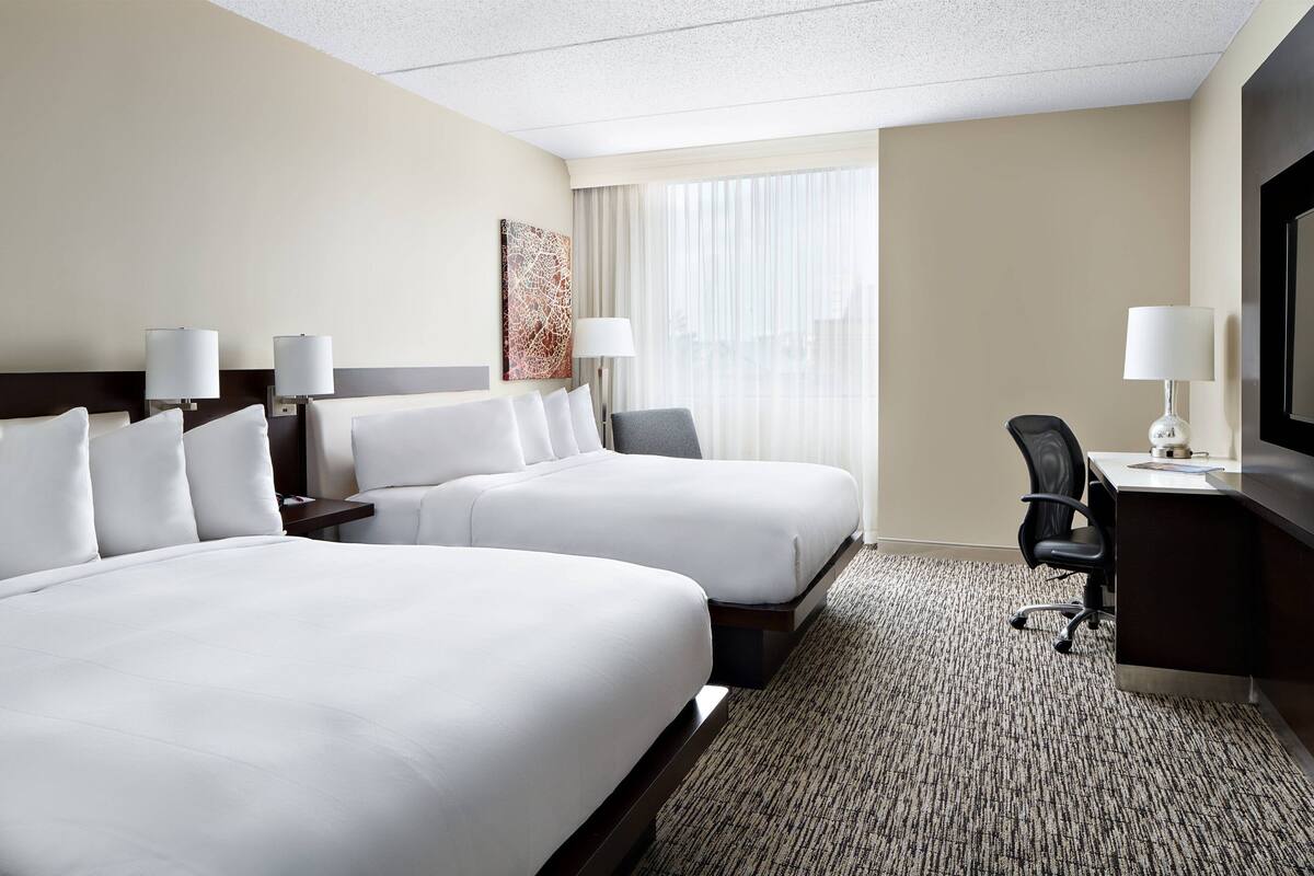 A hotel room with two beds, a desk, a chair, and a TV.