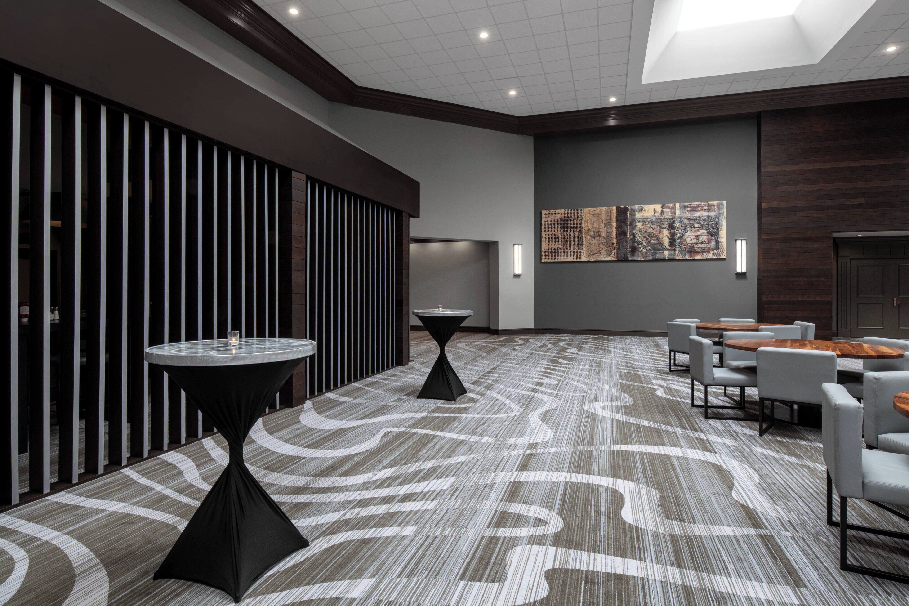 A modern hotel lobby with a patterned carpet, round tables, and a seating area.