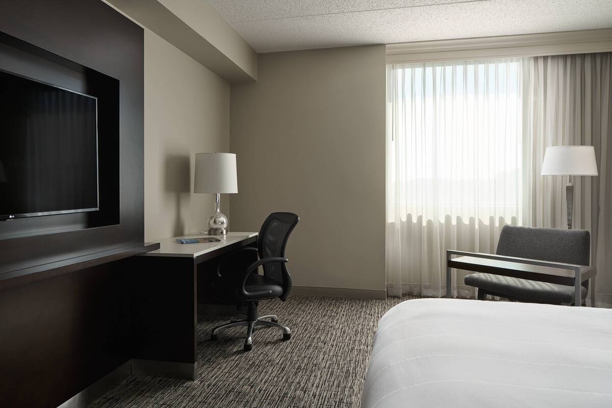 A hotel room with a bed, a desk, a chair, a TV, and a window with curtains.