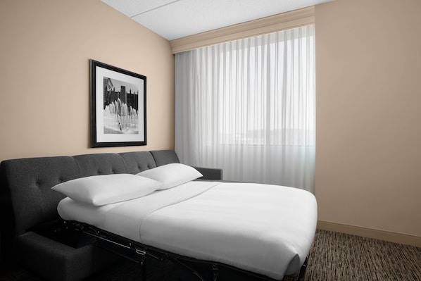 Une chambre d’hôtel avec un lit, un tableau encadré au mur et une fenêtre avec des rideaux légers.