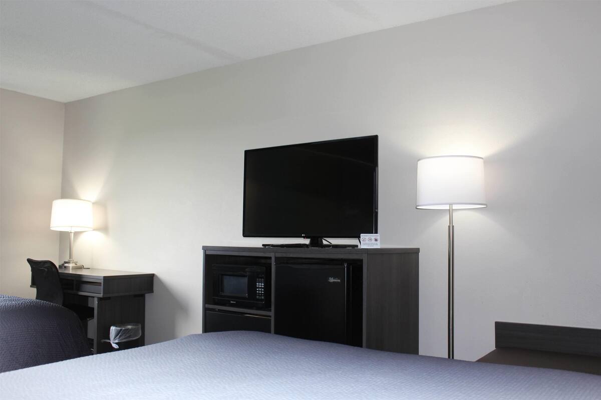 Hotelkamer met een bed, een bureau met lamp, een flatscreen-tv, een magnetron en een koelkast.