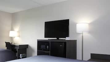 Quarto de hotel com cama, escrivaninha com luminária, TV de tela plana, micro-ondas e geladeira.