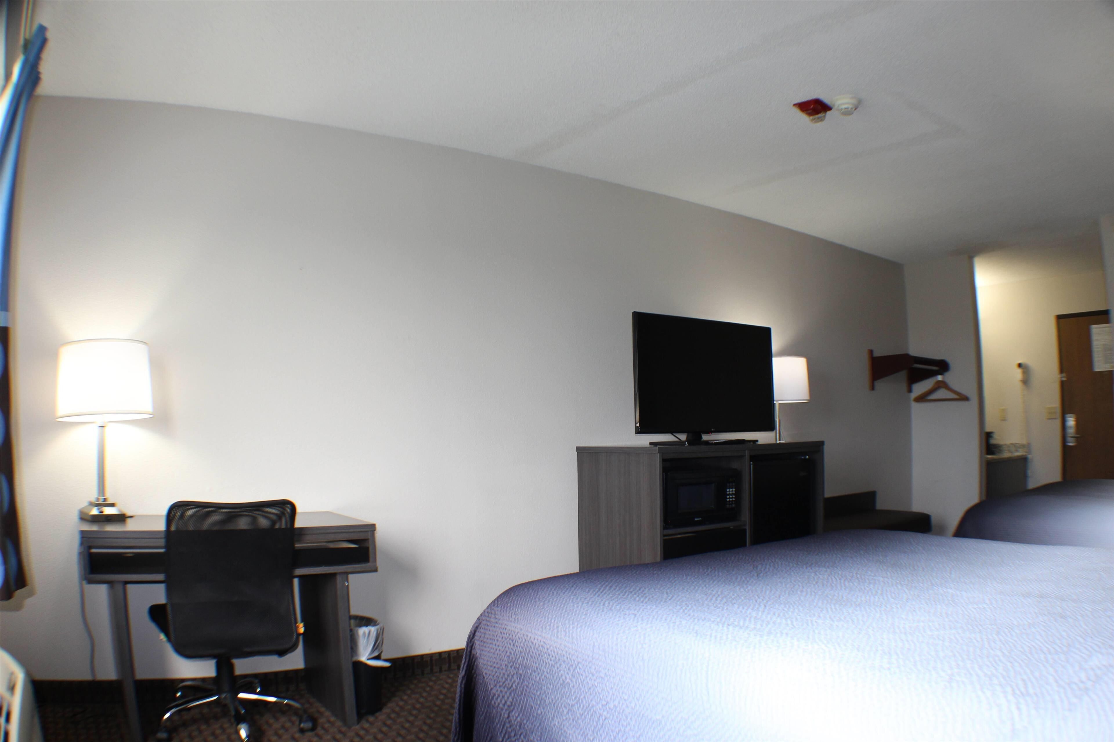 Ein Hotelzimmer mit Bett, Schreibtisch, Stuhl, Fernseher und einer Mikrowelle.