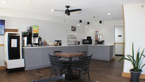 Une cuisine moderne avec des meubles gris, une table en bois et quatre chaises. On y trouve un four à micro-ondes, une machine à café et un réfrigérateur.