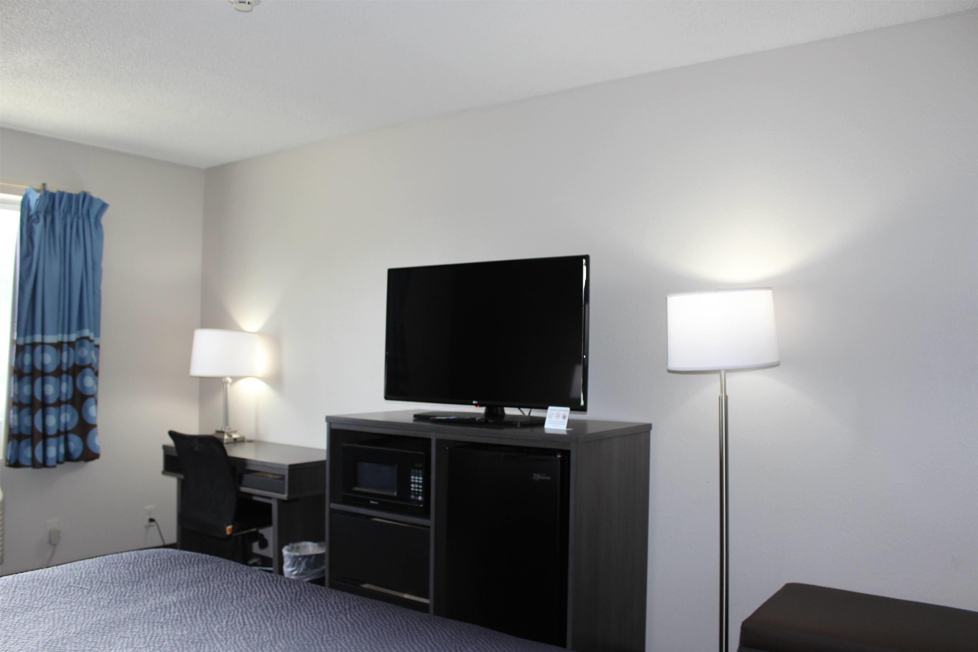 A hotel room with a bed, a desk with a computer, a flat-screen TV, a microwave, and a lamp.