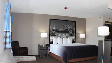 Una camera d'albergo con un letto grande, due comodini, una scrivania, una sedia, un divano e un quadro con una veduta sulla città.
