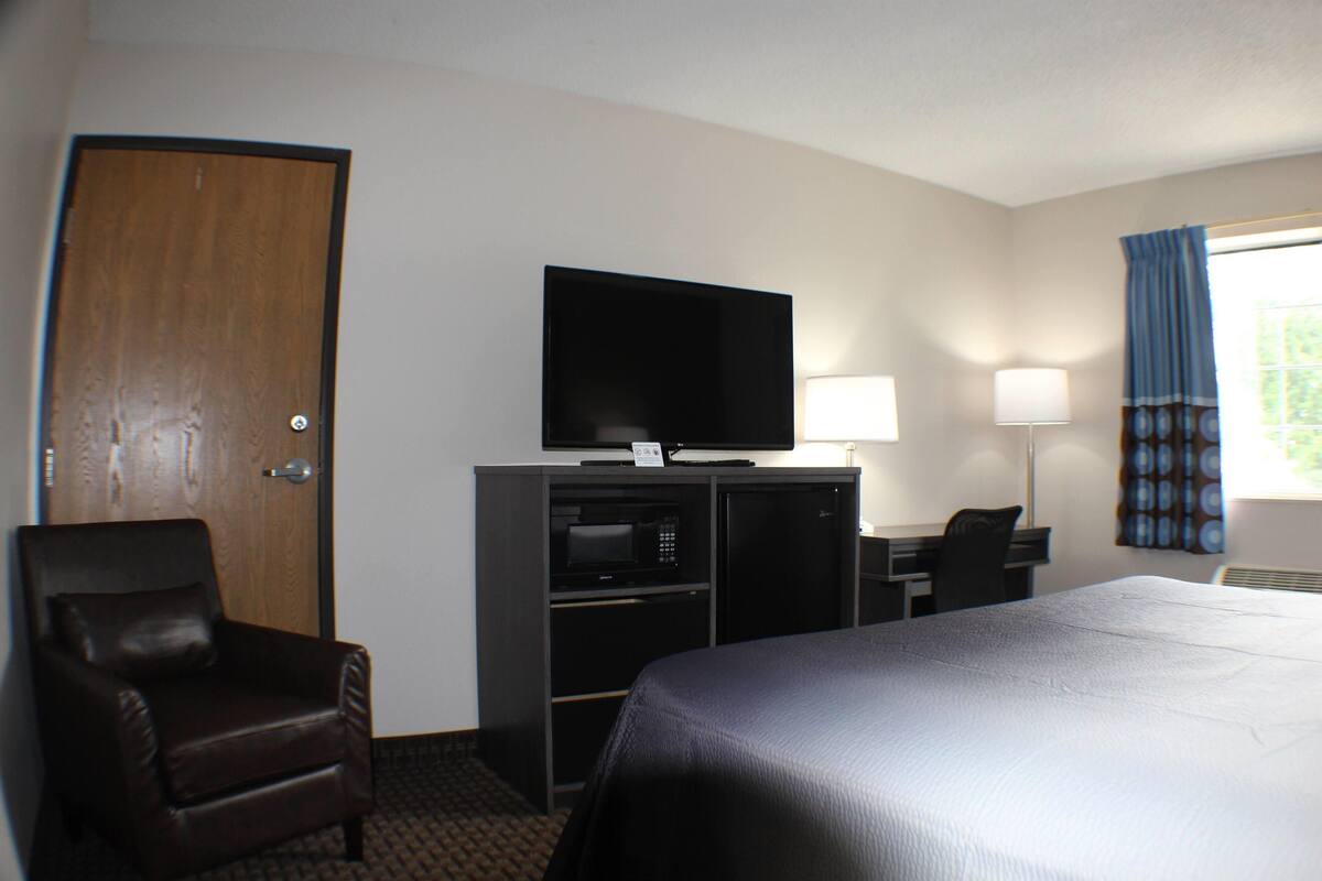 Een hotelkamer met een bed, een televisie, een bureau, een stoel en een deur.