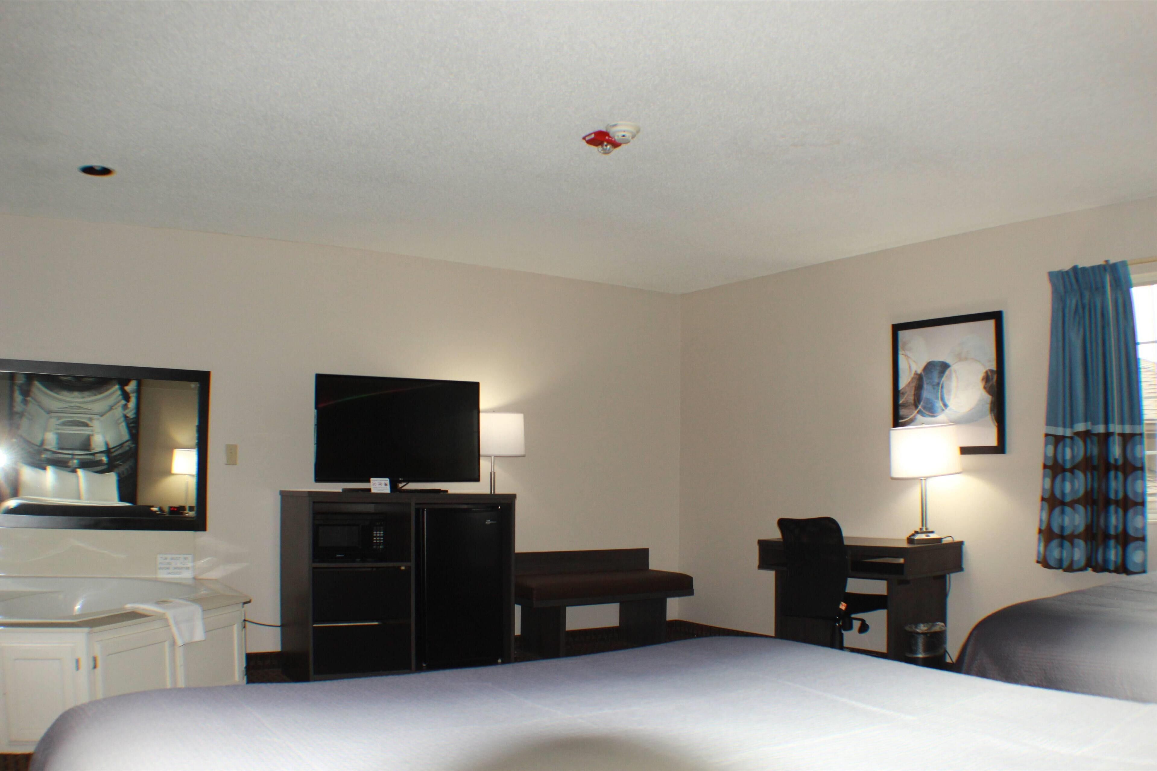 A hotel room with a bed, a desk, a television, a mirror, and a painting on the wall.
