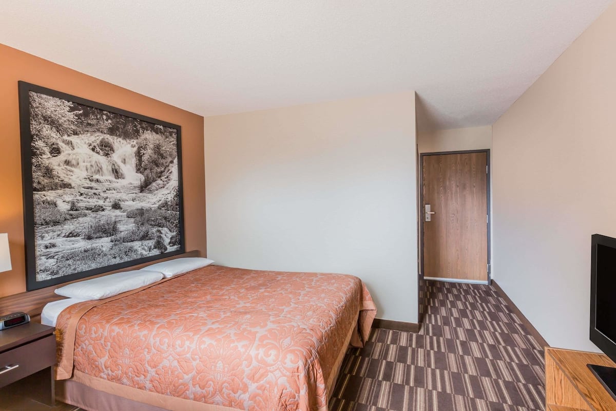 A hotel room with a large bed, a nightstand, a television, and a door leading to another room.