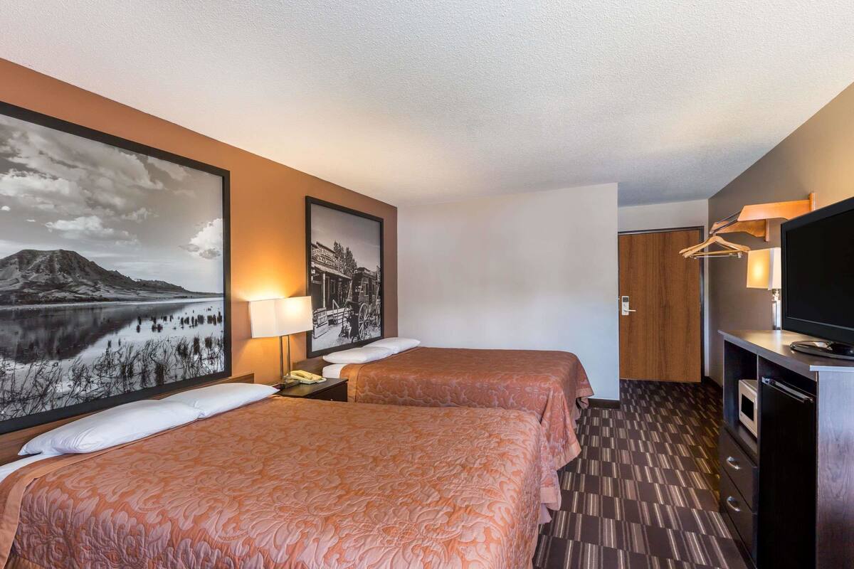 A hotel room with two beds, a TV, a desk with a lamp, and artwork on the walls.