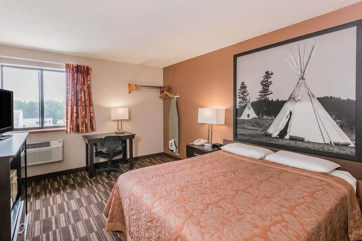 A hotel room with a bed, desk, chair, and a large window.