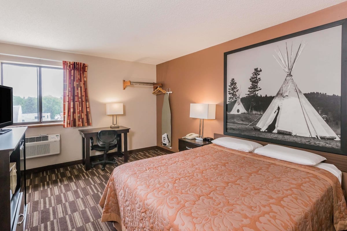A hotel room with a bed, desk, chair, and a large window.
