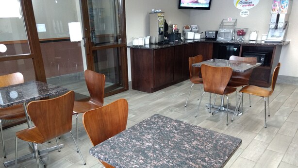 A restaurant with marble tables and wooden chairs, a counter with a coffee machine, and a television mounted on the wall. - Super 8 by Wyndham Madison (Madison)