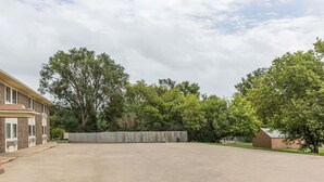 A spacious parking lot with a building on the left and a wooden fence in the center. - Super 8 by Wyndham Madison (Madison)
