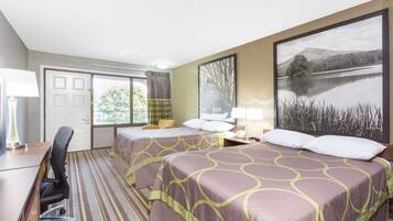 A hotel room with two beds, a desk, a chair, a lamp, and a large window with a view of trees and a lake.