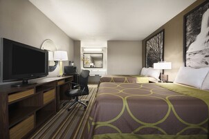 A hotel room with a large bed, a desk with a TV, a chair, and a desk lamp.