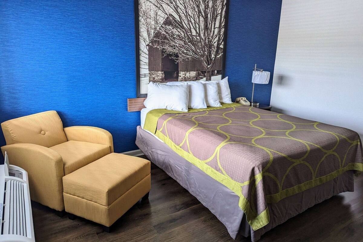 A hotel room with a bed, a chair, a nightstand, and a wall-mounted lamp.