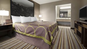 A hotel room with a large bed, a television, a desk with a lamp, and a bathroom visible through an open door. - Super 8 by Wyndham Wytheville (Wytheville)