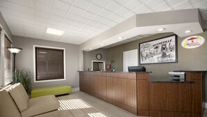 A reception area with a wooden desk, a clock, a framed picture of Wytheville, and a green bench. - Super 8 by Wyndham Wytheville (Wytheville)