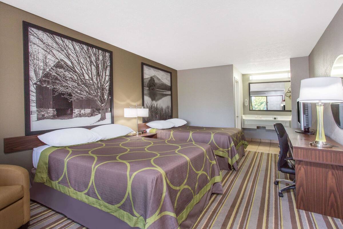 A hotel room with two beds, a desk, a chair, a TV, and a large window.