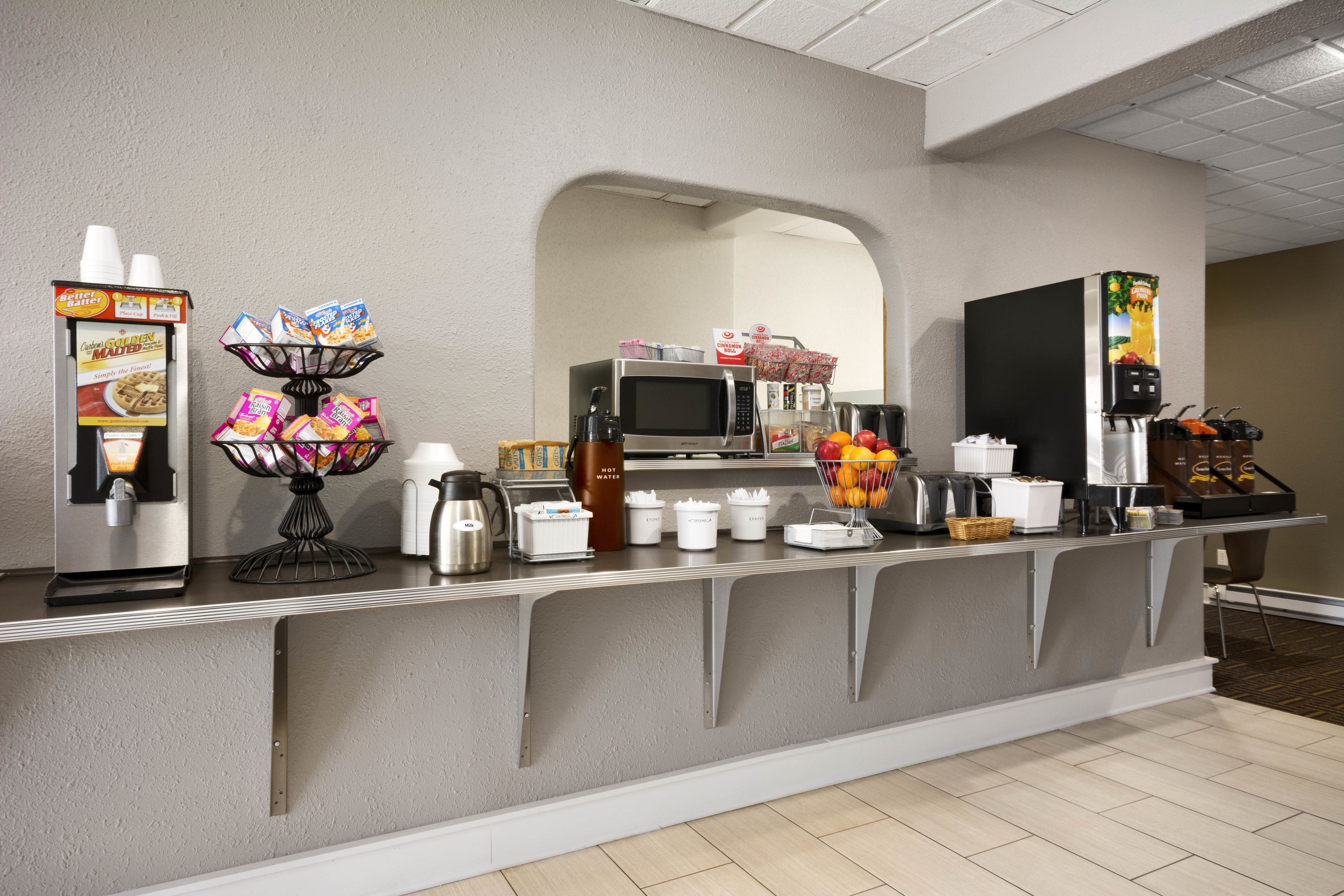 A self-service breakfast bar with a coffee machine, microwave, and various food items.