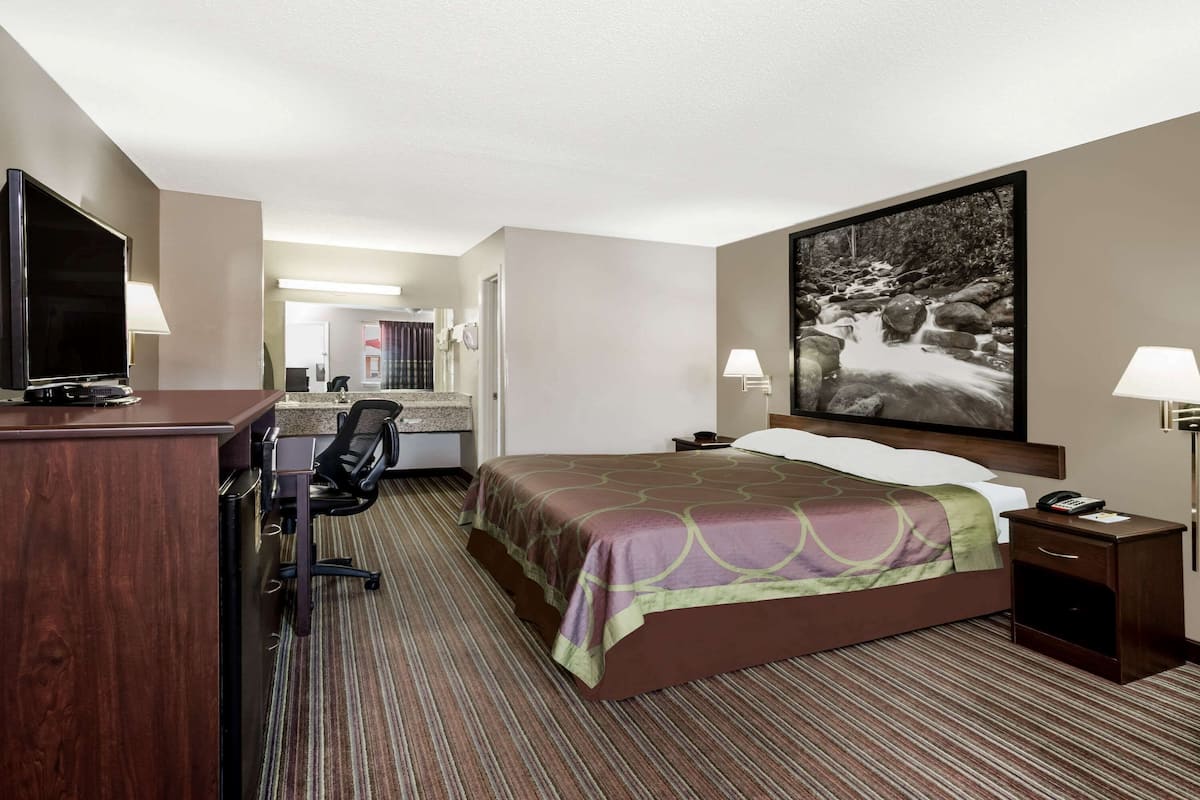 Una habitación de hotel con cama, escritorio, silla, televisor y un cuadro en la pared.