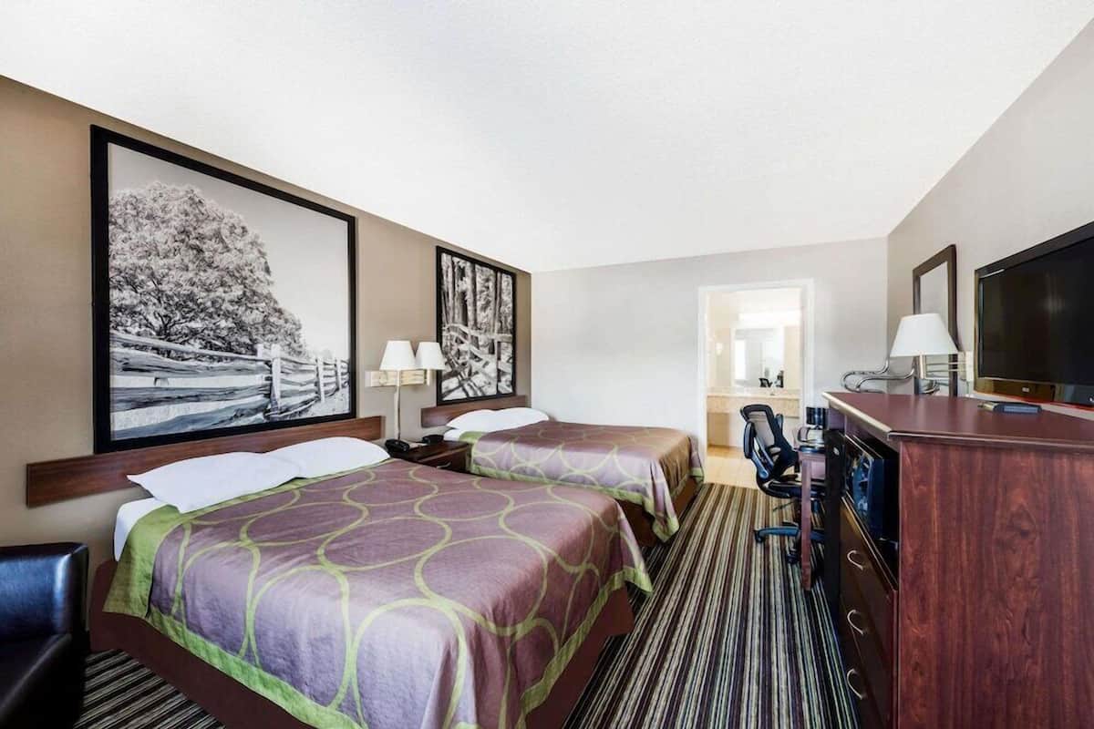 Habitación de hotel con dos camas, un escritorio, un televisor y obras de arte en las paredes.