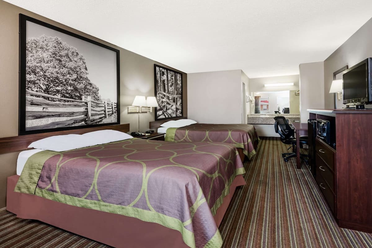 Habitación de hotel con dos camas, un escritorio, una silla, un televisor y obras de arte en las paredes.