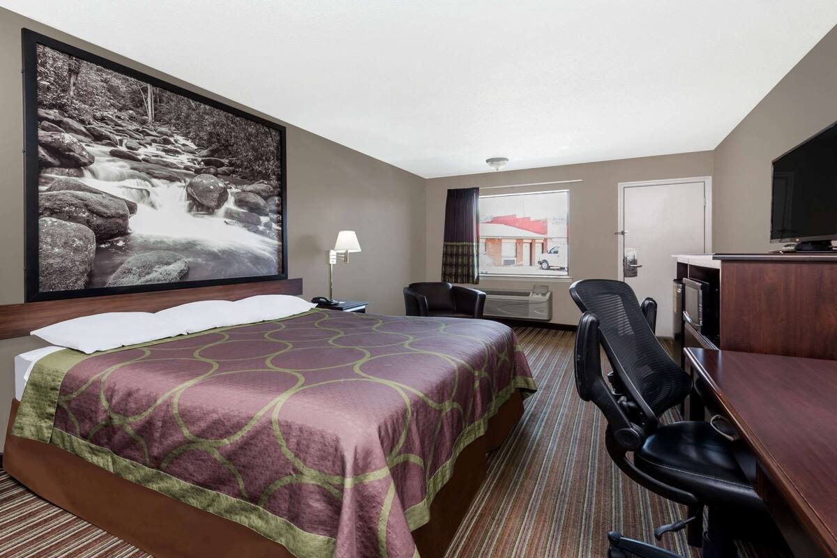 Habitación de hotel con una cama grande, un escritorio con silla, un televisor y una ventana con vistas a un edificio.