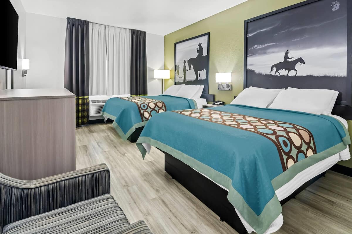A hotel room with two beds, a desk, a TV, and artwork on the walls.