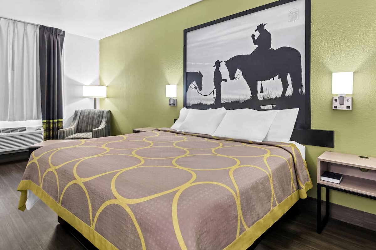A hotel room with a large bed, a chair, a desk, and a wall-mounted lamp.