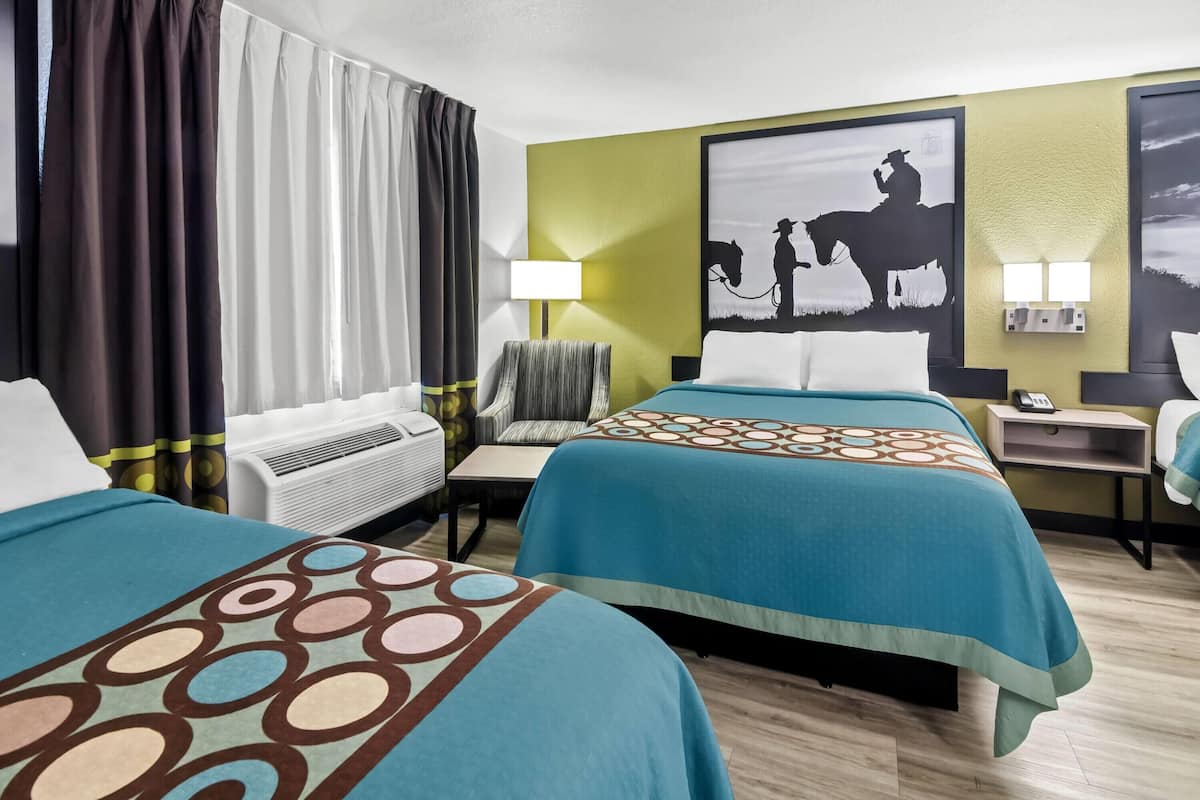 A hotel room with two beds, a desk, a chair, a lamp, and a wall-mounted air conditioner.