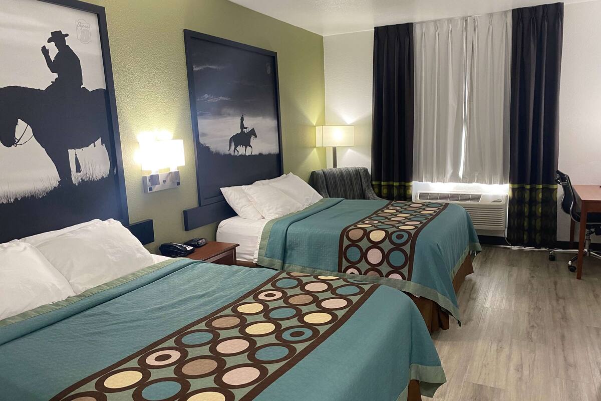 A hotel room with two beds, a nightstand, a lamp, a chair, and a window with curtains.