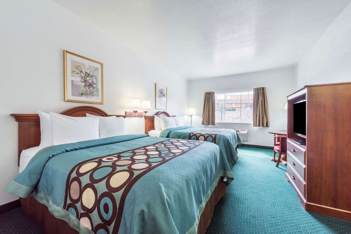 A hotel room with two beds, a TV, a desk, and a window with curtains.