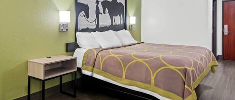 A hotel room with a bed, a nightstand, a table, and a wall-mounted painting of a cowboy and horse.