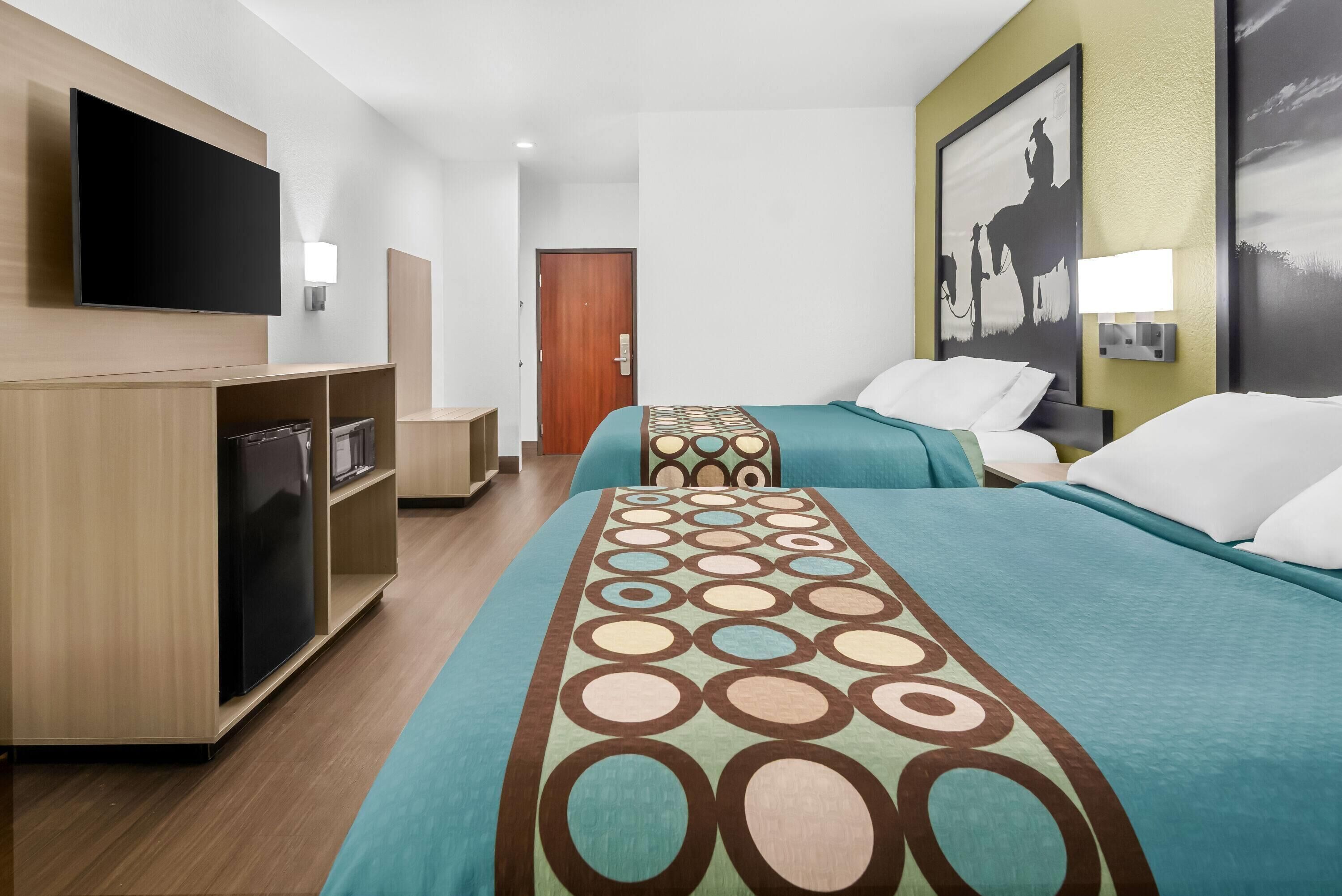 Ein Hotelzimmer mit zwei Betten, einem Fernseher, einem Schreibtisch und einer Tür.