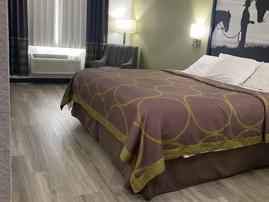 Habitación de hotel con cama, una silla, una lámpara y un cuadro en la pared.