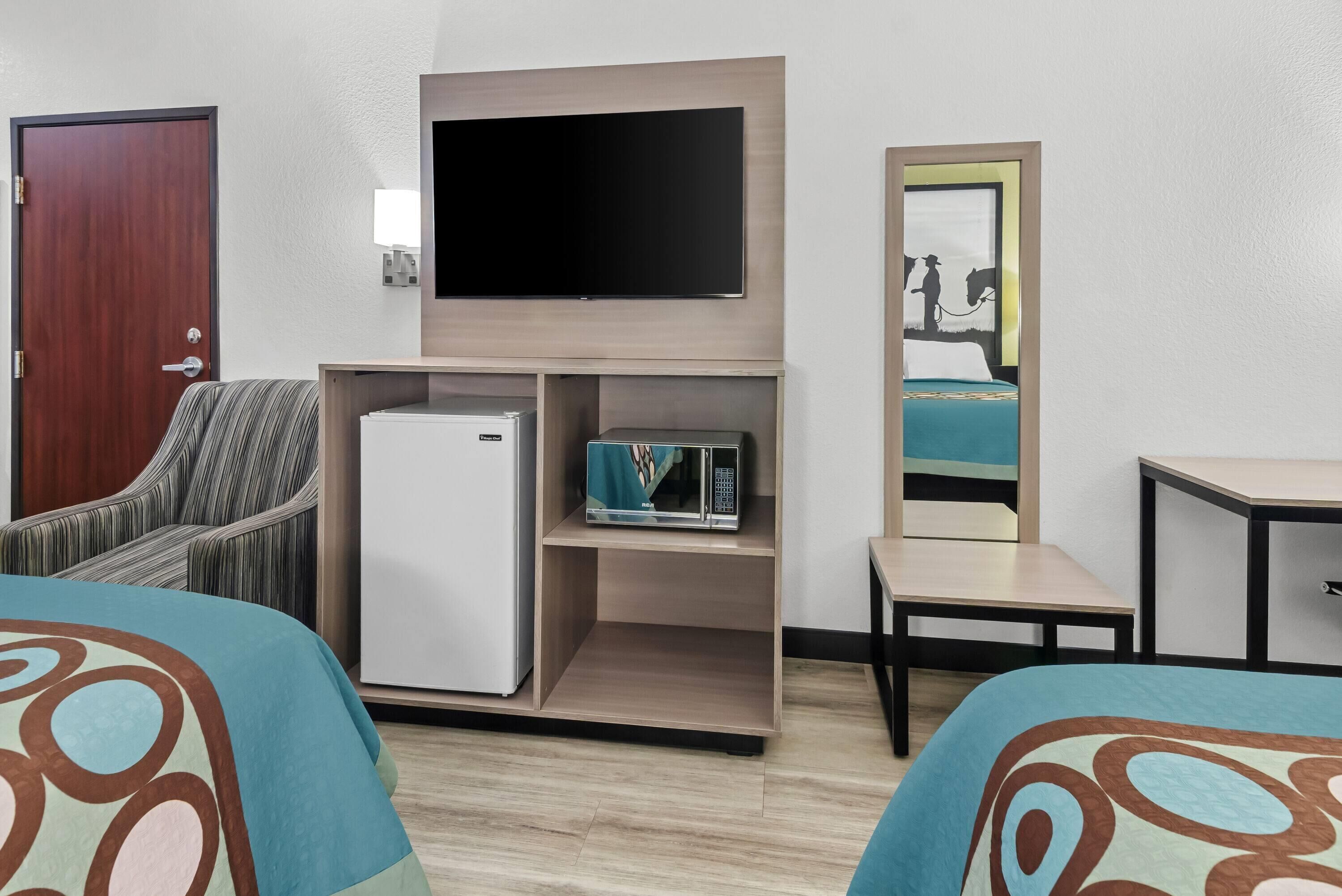 A hotel room with a bed, a television, a microwave, a refrigerator, a chair, and a small table.