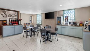 A modern dining area with a kitchen counter, seating, and a flat-screen TV. - Super 8 by Wyndham Fredericksburg (Fredericksburg)