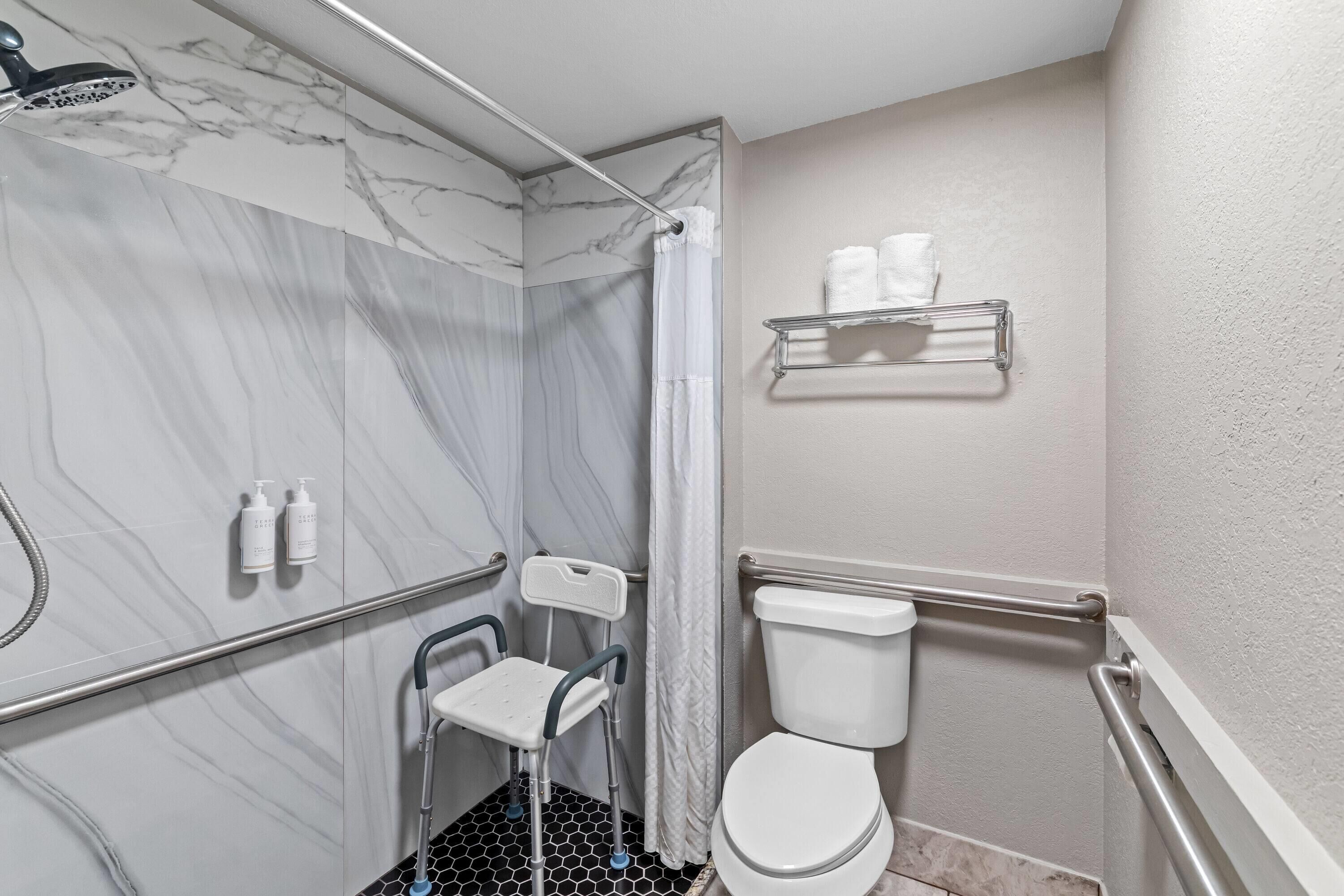 Een badkamer met douche, toilet en handgrepen.