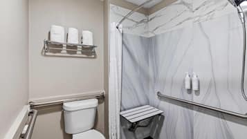 A bathroom with a toilet, a shower with a marble wall, a towel rack with towels, and a small shelf with toiletries.