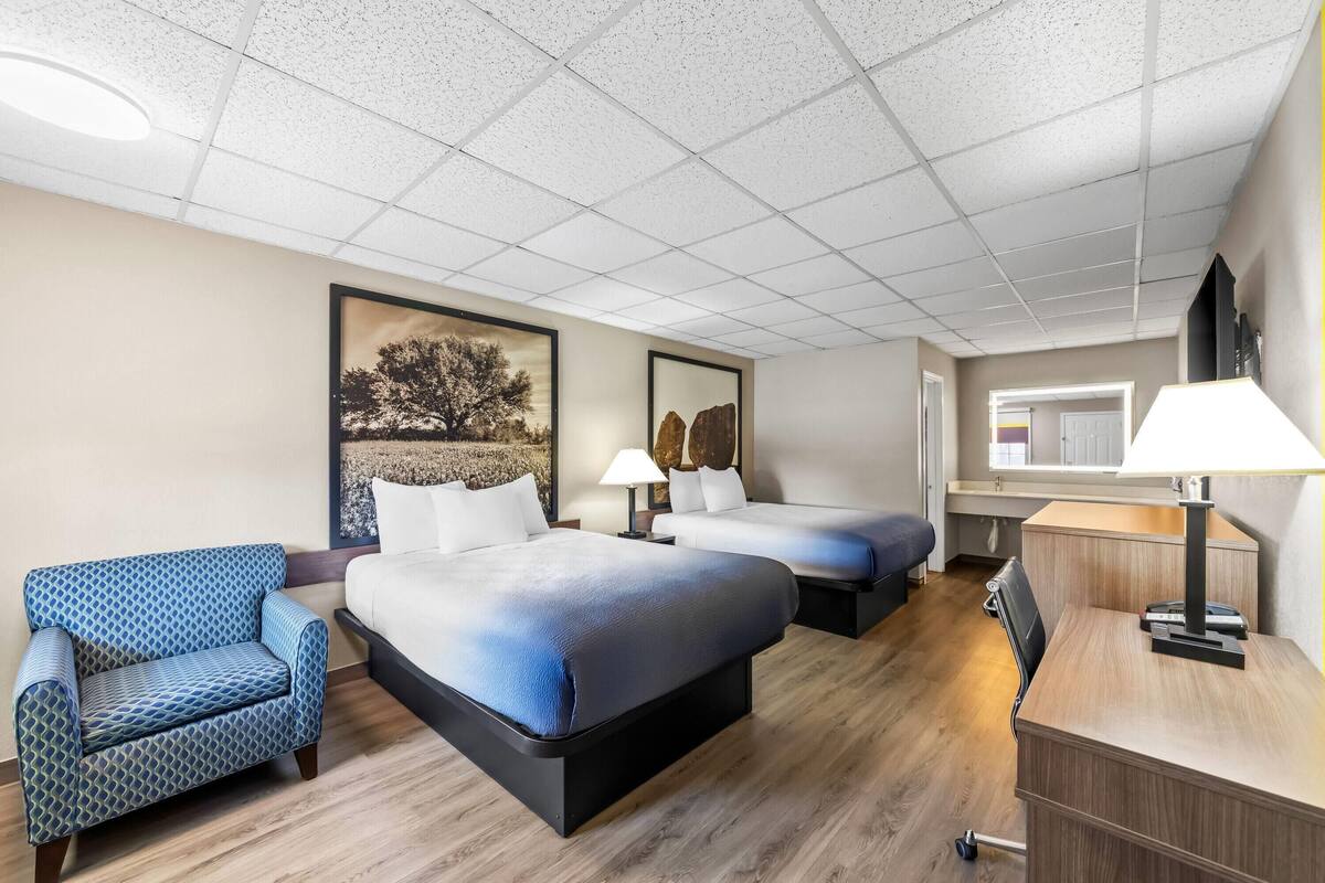 A hotel room with two beds, a sofa, a desk, and a lamp.