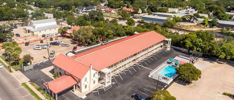 An aerial view of a building with a red roof, a parking lot, and a swimming pool.