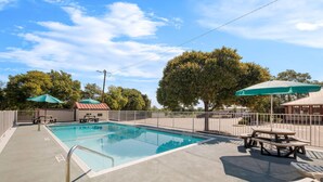 A swimming pool with a metal ladder, picnic tables, and umbrellas. - Super 8 by Wyndham Fredericksburg (Fredericksburg)