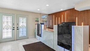 A reception area with a modern design, featuring a reception desk, a large flat-screen TV, and a wooden panel wall. - Super 8 by Wyndham Fredericksburg (Fredericksburg)