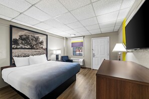 A hotel room with a bed, bedside table, lamp, and a large painting on the wall. - Super 8 by Wyndham Fredericksburg (Fredericksburg)