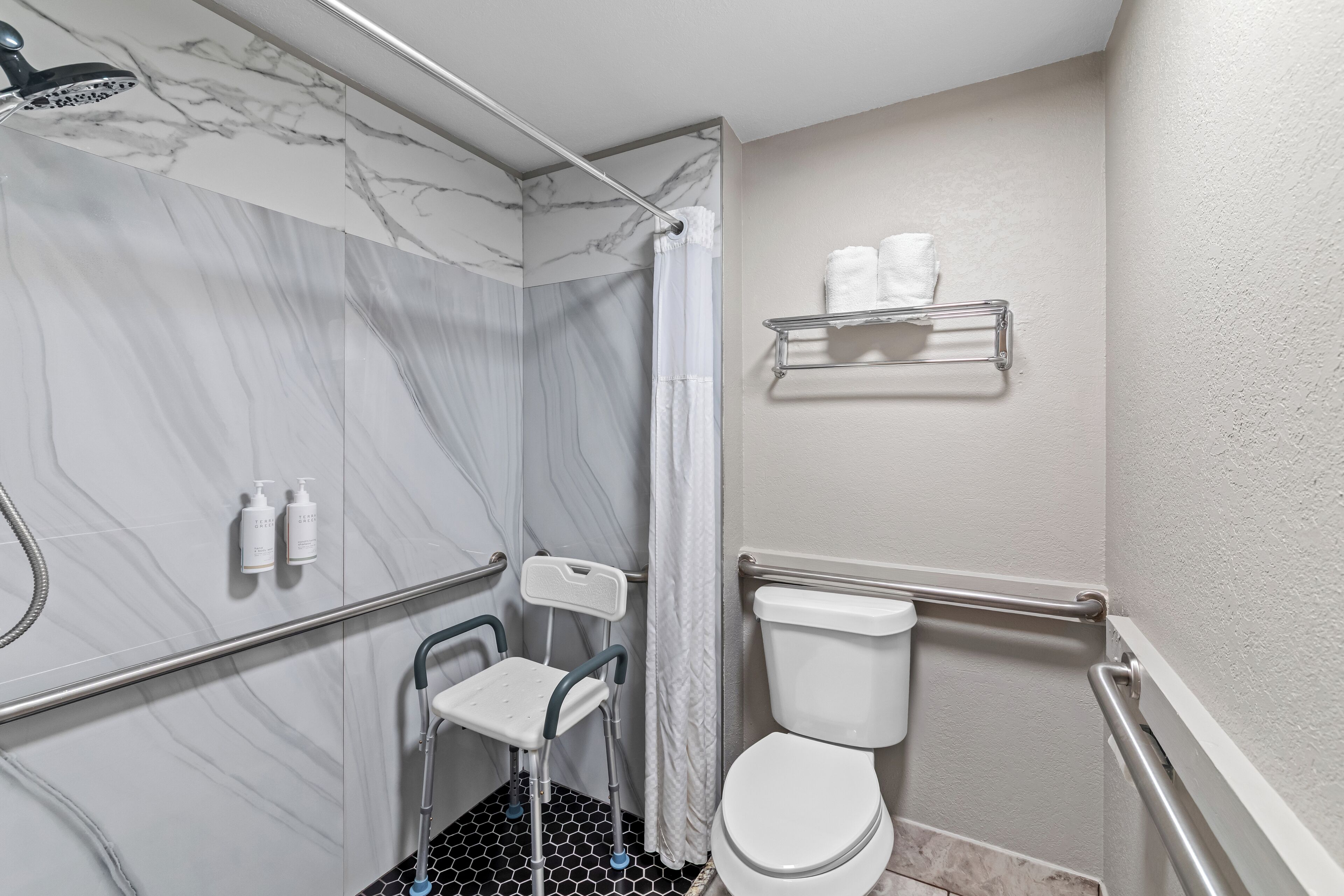 Un baño con ducha, inodoro y barras de apoyo.