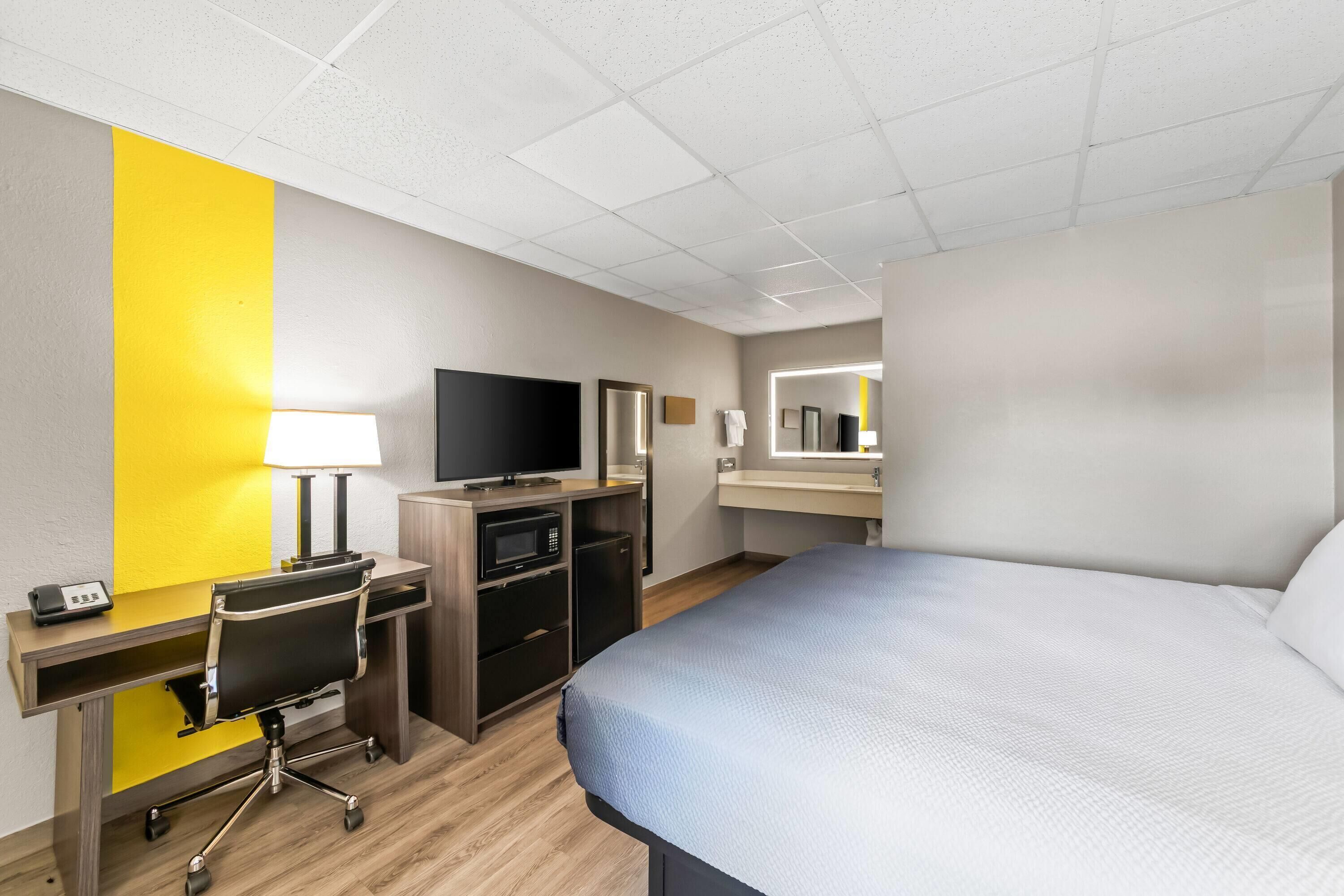 Une chambre d’hôtel équipée d’un lit, d’un bureau, d’une télévision, d’un four à micro-ondes et d’un miroir.